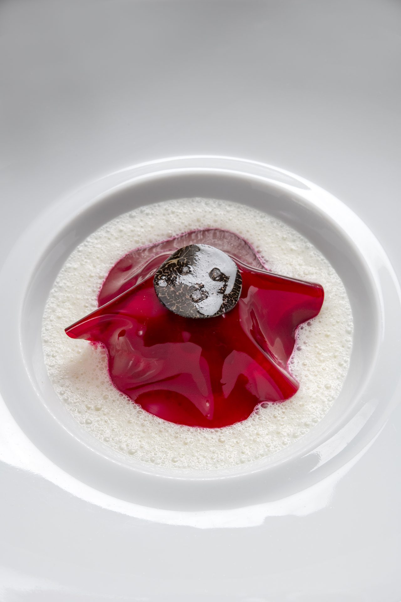 Beetroot consomme with caviar in a white bowl