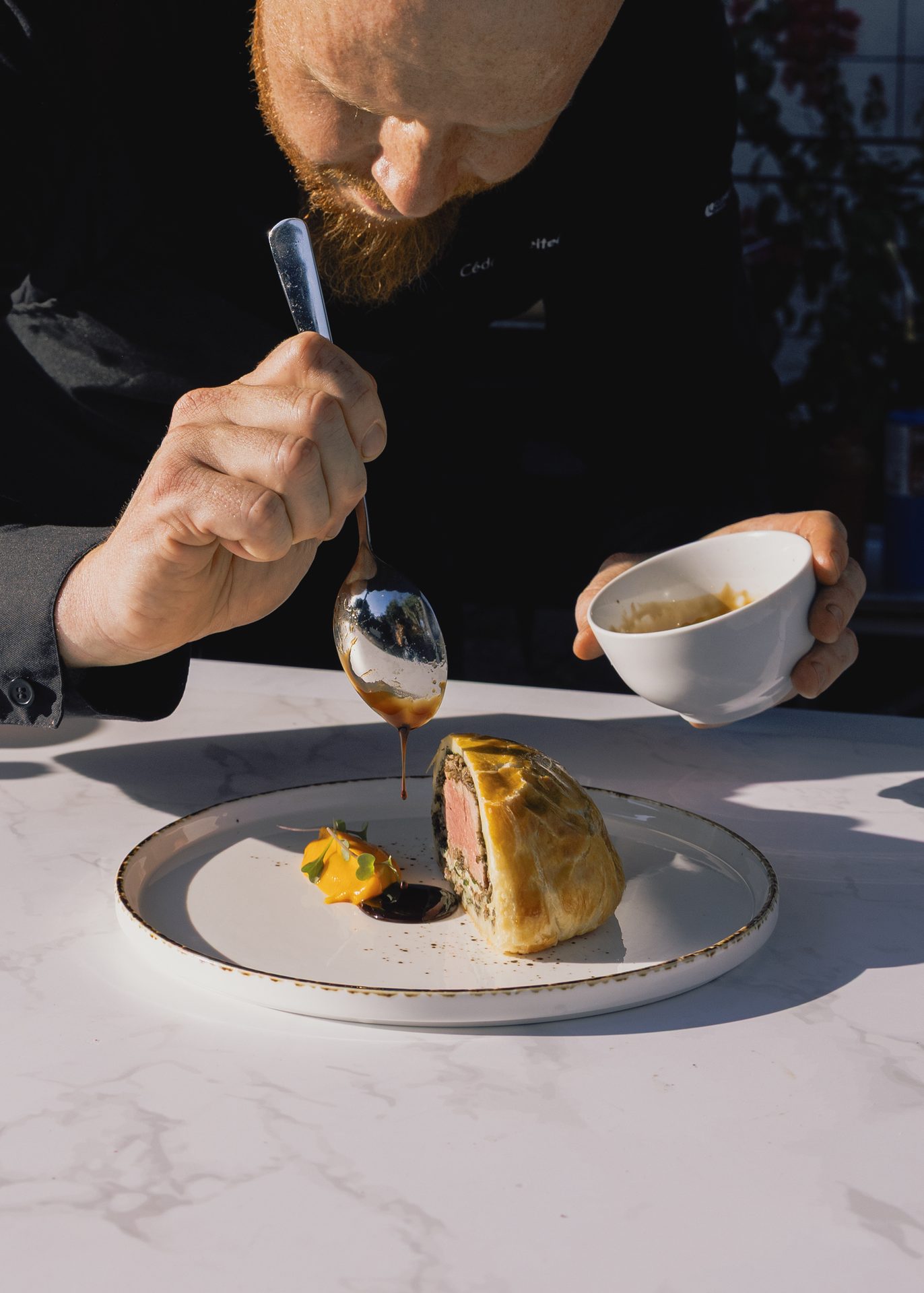 Sauce being spooned over a plated course on a marble counter